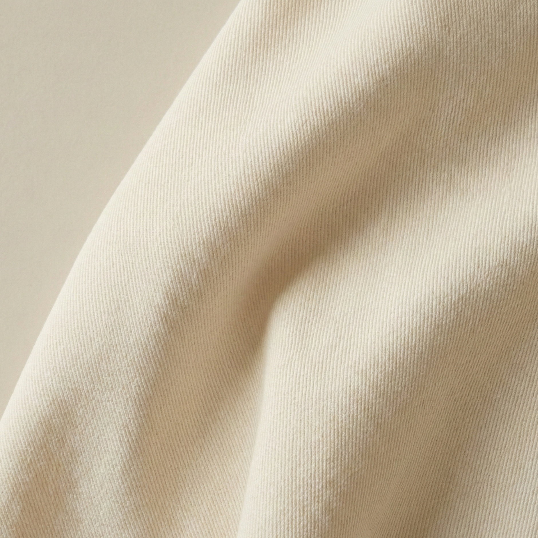Close-up texture of beige soft cotton twill fabric showing a detailed diagonal weave pattern and soft, natural folds.