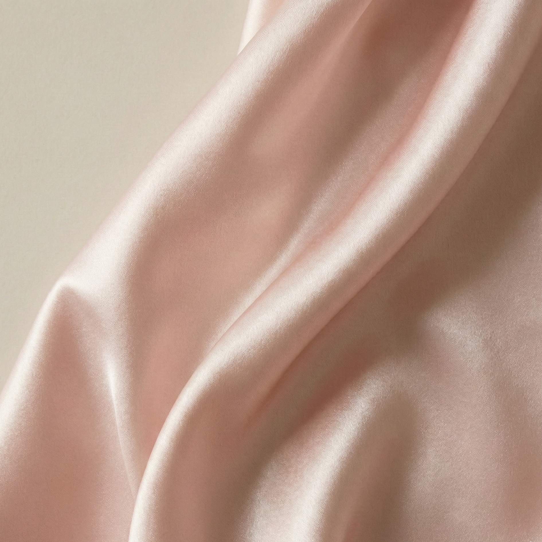 Close-up texture of draped pink silk satin fabric with soft lighting highlighting the glossy sheen and folds.